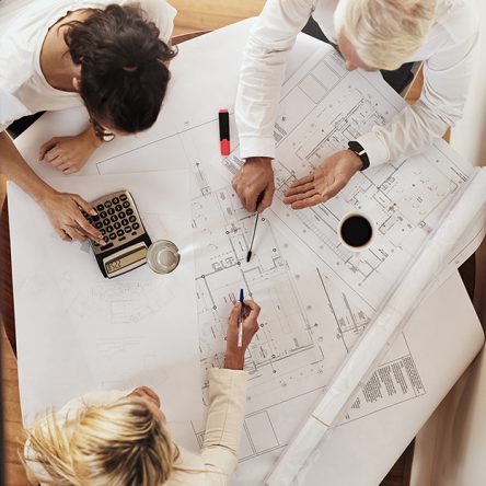 High angle shot of a group of architects working together on blueprints of a house around a table inside of a building.